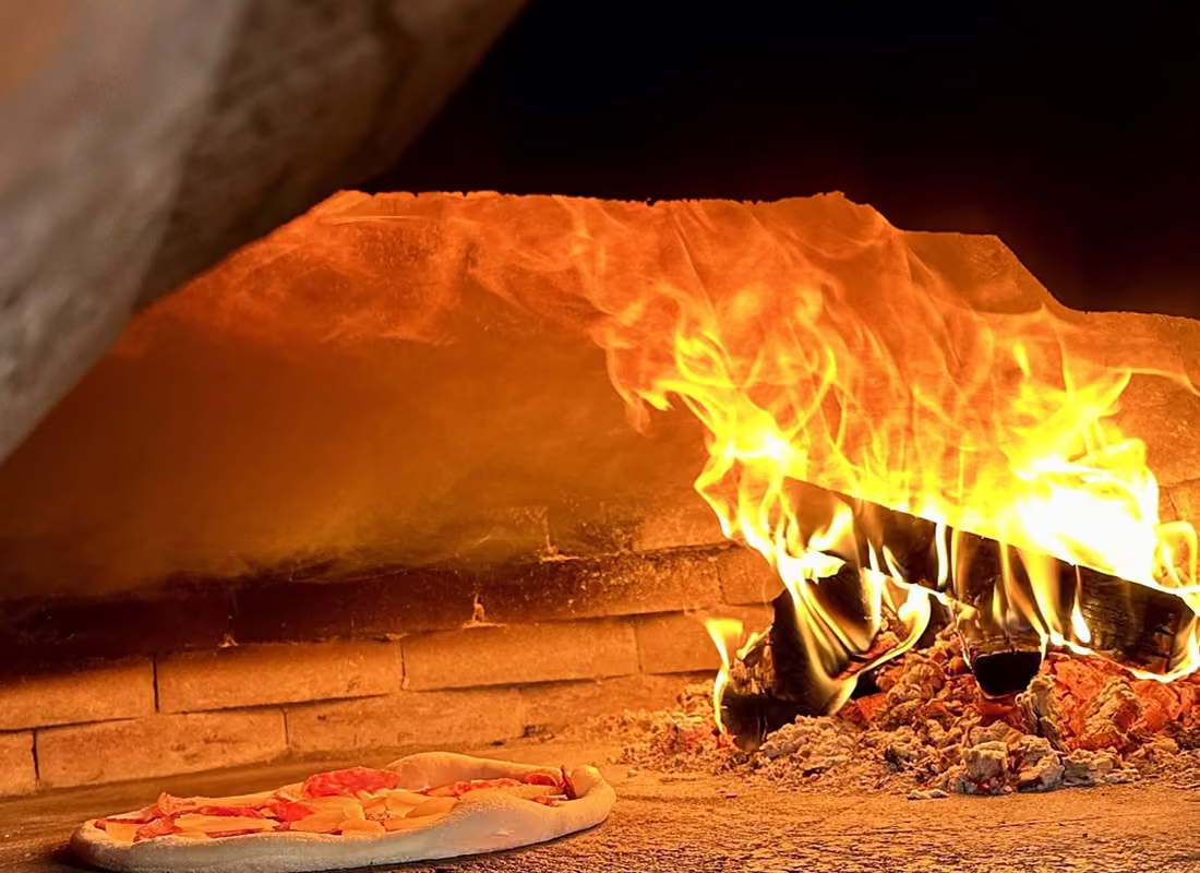 Ogień w piecu opalanym drewnem, na dnie pieca piecze się pizza